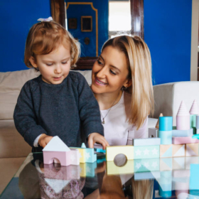 Beautiful young mother and cute baby daughter playing with construction toys in their living room.